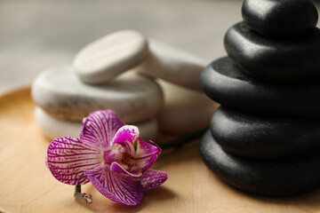 Fototapeta na wymiar Spa stones and orchid flower on wooden plate, closeup