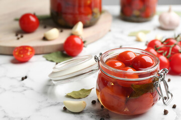 Glass jar of pickled cherry tomatoes and ingredients on white marble table. Space for text