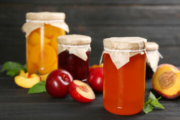 Glass jar of peach jam and fresh fruits on black wooden table