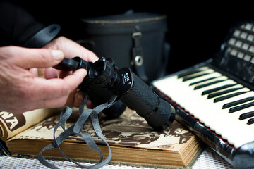hands holding vintage binoculars over an antique book and an accordion