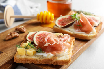 Delicious sandwiches with figs, proscuitto and cheese on light table, closeup