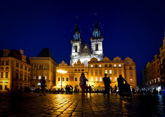 Obraz premium Tourists in silhouette sightsee late at night in Old Town Square under the lighted towers of Our Lady Before Tyn Church in the Prague, Czechia.