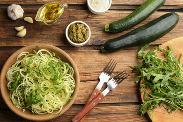 Tasty zucchini pasta with arugula, sauce and ingredients on wooden table, flat lay