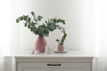 Beautiful eucalyptus branches, candle and bird figures on chest of drawers indoors. Interior element