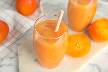 Tasty persimmon smoothie with straw on white table, closeup