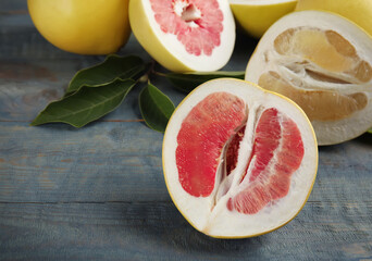 Fresh cut pomelo fruits with leaves on blue wooden table, closeup