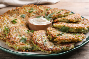 Delicious zucchini fritters with sour cream served on wooden table, closeup