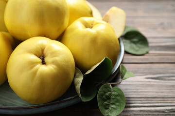 Fresh ripe organic quinces with leaves on wooden table, closeup