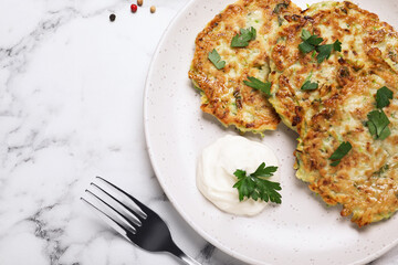Delicious zucchini fritters served on white marble table, flat lay