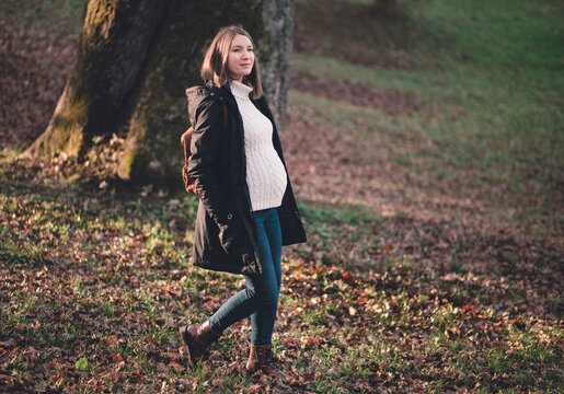 Pregnant happy young woman walking outdoors in autumn park