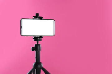 Smartphone with blank screen fixed to tripod on pink background. Space for text