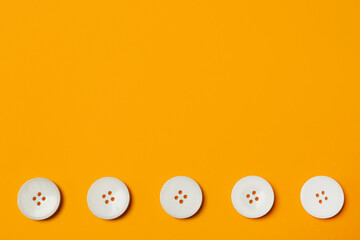 Line of white buttons on orange background, flat lay. Space for text