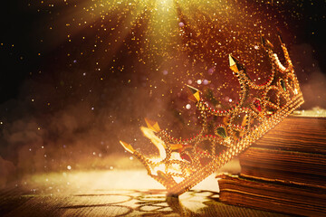 Fantasy world. Beautiful golden crown and old books lit by magic light on table