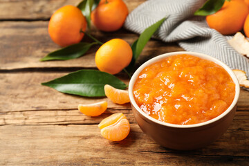 Tasty tangerine jam in bowl on wooden table. Space for text