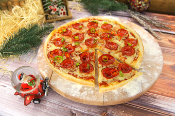 Italian pepperoni pizza served on wooden plate and table with Christmas new year decoration on background. Fast food dish with salami sausages, red and green chili pepper slices and mozzarella cheese
