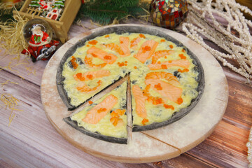 Italian black dough pizza served on wooden plate and table with Christmas new year decoration on background. Fast food seafood dish with red fish salmon slices, black tiger shrimps and red caviar
