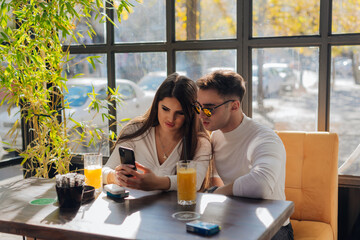 Friends socializing, having fun, and laughing drinking coffee in coffeehouse while fooling around. Male and female friends Taking pictures together on a sunny day..