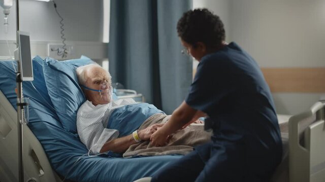Hospital Ward: Friendly Head Nurse Connects Finger Heart Rate Monitor or Pulse Oximeter to Elderly Patient Wearing Oxygen Mask Resting in Bed