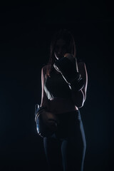 Fototapeta na wymiar Silhouette portrait of a sexy fit woman posing in dark contrast with boxing gloves