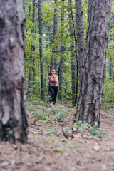 Fototapeta premium Young caucasian girl jogging in the forest seen from far away.