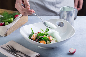 Chef completes the cooking salad and add with a white sauce to red fish and vegetables.