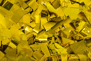 Confetti in shiny gold color lying as a background, golden foil particles flakes texture structure