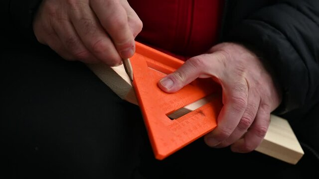 Carpenter makes a cut mark with his pencil and a ruler or set square tool on a piece of wood
