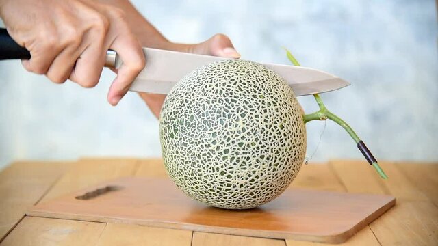 The man use knife split the orange melon on wood plate