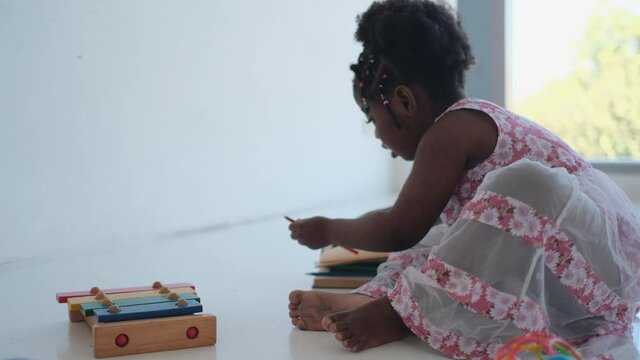 African American girl play with book near xylophone and she look fun and happy in front of glass window with morning light. Concept of happiness lifestyle for stay at home during covid pandemic.
