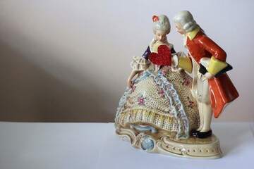 Porcelain figurines couple with a male handling a Valentine's Day heart card to a female background with a copy space