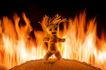 Eine Voodoo Puppe steht vor einem Feuer. Nadeln stecken in ihr.