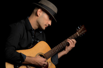 Image of a man in the studio with a hat playing the guitar.