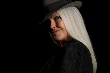 Image of a beautiful mature woman with platinum blonde hair, wearing a hat. Studio image with a black background.
