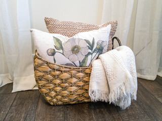 Throw pillows and blanket inside a wicker basket against dark brown wood floor