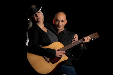 Image of a man and woman sitting in a dark room holding a guitar, creating art and music.