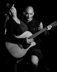 Image of a man and woman sitting in a dark room holding a guitar, creating art and music.