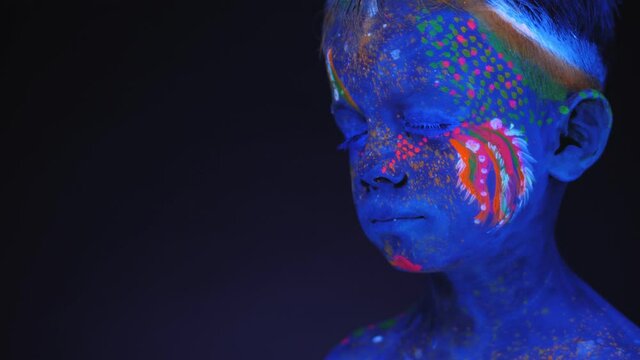 Portrait of a small child with an ultraviolet pattern on the face that glows under fluorescent lighting.