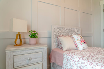 Bed with decorative head board against white panelled wall of feminine bedroom