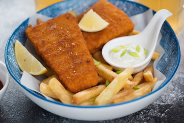Deep-fried breaded fish fillet with french fries and dips in a blue bowl, close-up, studio shot