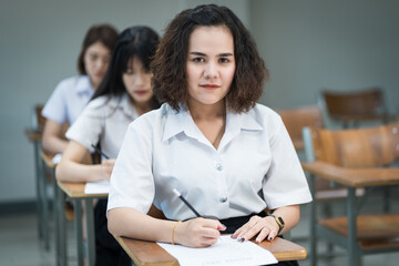 Portrait of cheerful Asian female college students writing and studying in the classroom. Selective focus teenage university students studying in classroom.