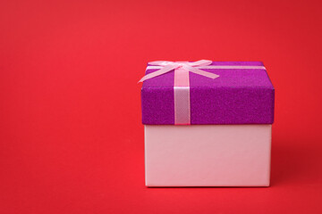 Gift box with pink ribbon on red background.