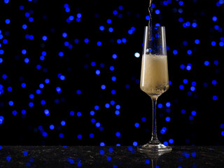 A stream of sparkling wine pours into a tall glass against a background of blue bokeh.