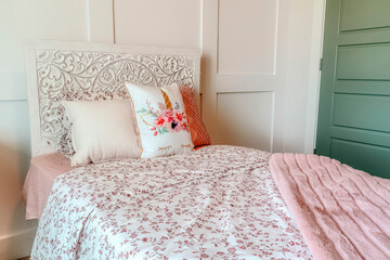 Fluffy pillows against headboard of bed with floral bedsheet and pink blanket