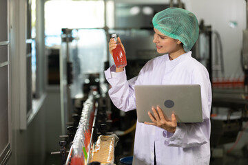 young woman factory worker looking basil seed drink and using laptop computer for checking quality...