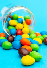 Candies scattered from glass jar on blue background. Close up.