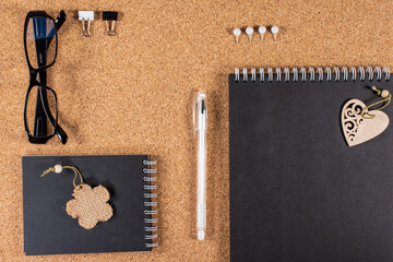 Black glasses and notebooks on a cork board and some office supplies and jewelry