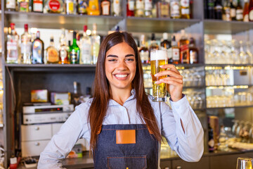 Beautiful smiling female Bartender serving a draft beer at the bar counter , shelves full of bottles with alcohol on the background