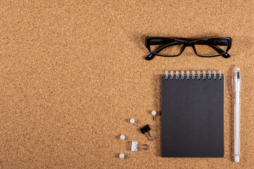 Black glasses and a black notebook on a cork board