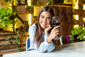 Image of cute pretty young woman sitting in cafe holding glass and drinking wine. portrait of a beautiful wine tasting tourist woman.