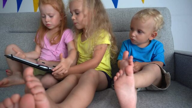 Children kids share tablet computer sitting on sofa. Sisters and brother